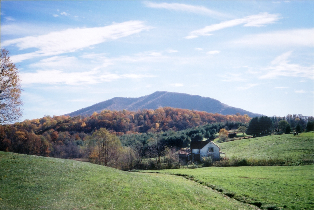 A white farmhouse nestled in green pastures beneath an autumn-colored mountain in the High Country